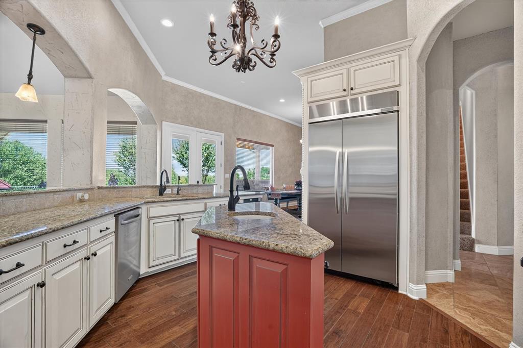 100 Canyon Ridge Trail Aledo, TX 76008 - Photo 11 of 38 Elegant kitchen featuring cream-painted cabinetry with dark hardware, granite countertops, a custom red-painted island with seating, stainless steel refrigerator and appliances, pendant lighting, arched doorways, recessed ceiling details, and warm wood-finish flooring throughout