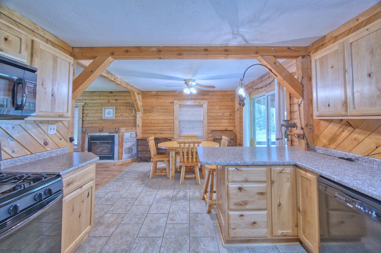 7349 Lax Road Embarrass, MN 55732 - Photo 7 of 36 Kitchen with light brown cabinets, black appliances, a peninsula, rustic walls, and a glass covered fireplace