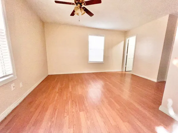 an empty room with wooden floor fan and windows