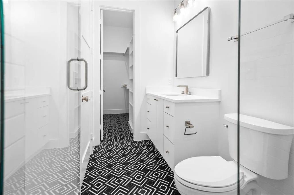 309 Kaye Street Coppell, TX 75019 - Photo 24 of 36 Modern bathroom featuring black and white patterned floor tile, white vanity with integrated sink, rectangular framed mirror, and glass shower enclosure