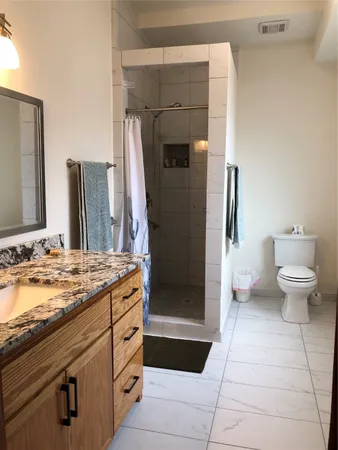 a bathroom with a granite countertop sink a toilet a mirror and shower