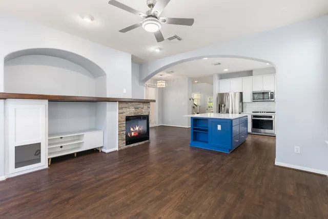 a living room with stainless steel appliances kitchen island a fireplace wooden floor and furniture