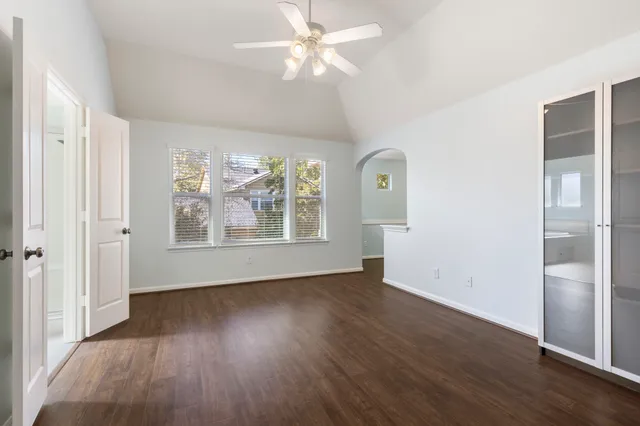 an empty room with wooden floor chandelier fan and windows