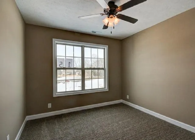 an empty room with chandelier fan and windows