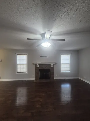 a view of an empty room with wooden floor fireplace and a window