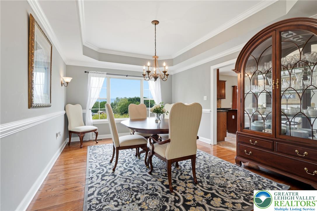 245 East Dell Road Bath, PA 18014 - Photo 11 of 99 A formal dining area showcases a warm hardwood floor, elegant crown molding, and a charming chandelier, all bathed in natural light from the large windows.