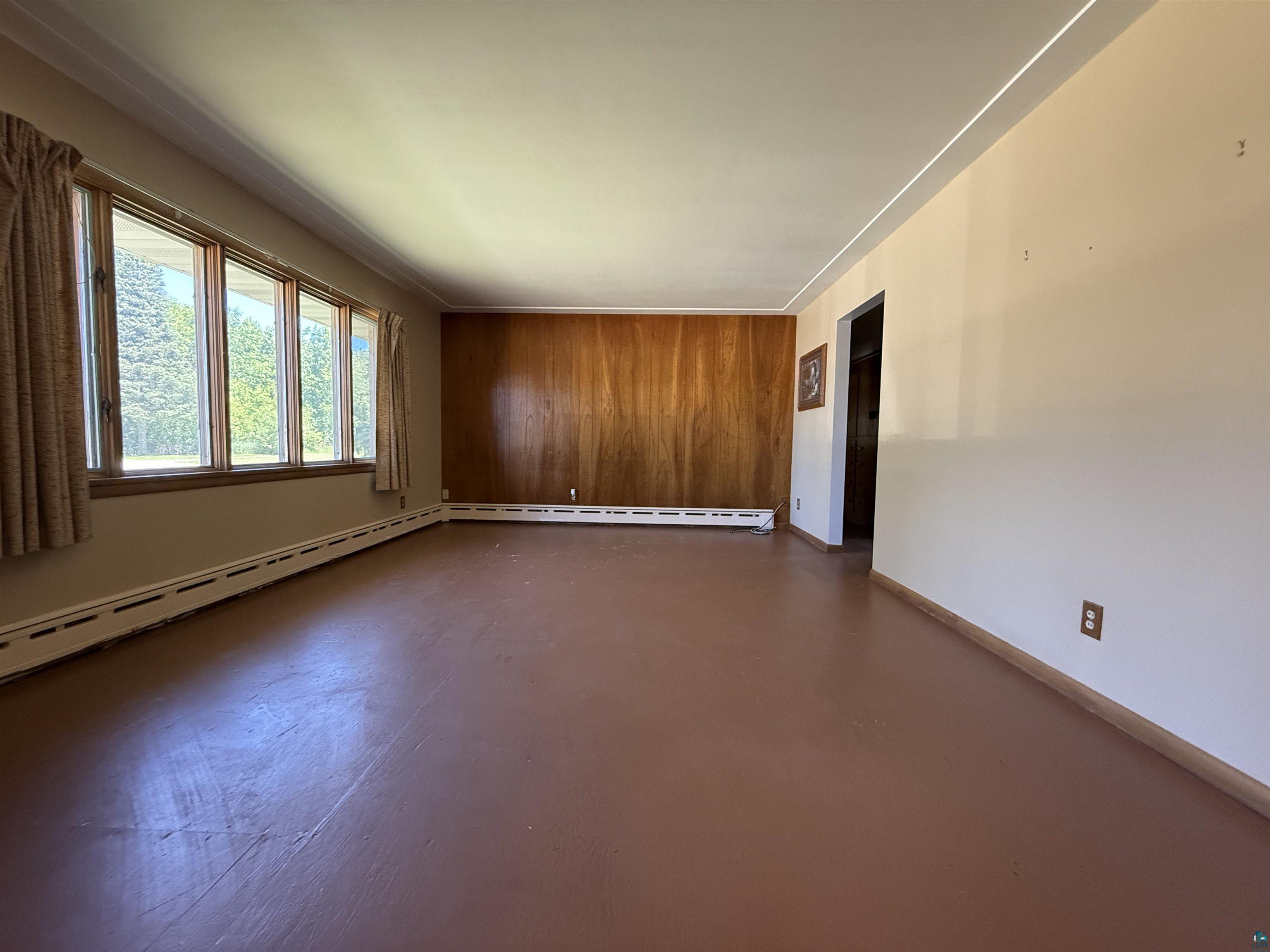 607 3rd Street Northeast Chisholm, MN 55719 - Photo 5 of 32 Spacious interior featuring a multi-pane window, hardwood wall paneling, baseboard heating, and wood-finish flooring