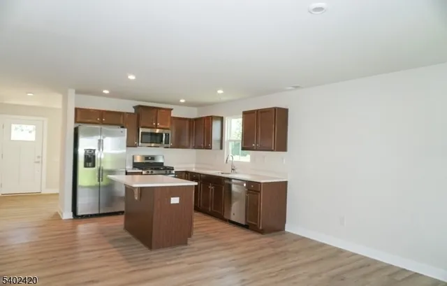 a kitchen with stainless steel appliances granite countertop a stove top oven a sink dishwasher and a refrigerator with wooden floor