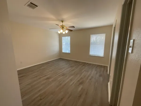 an empty room with wooden floor fan and windows