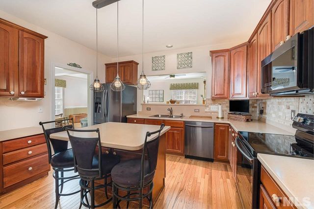 a kitchen with stainless steel appliances granite countertop a sink a stove a refrigerator cabinets and chairs