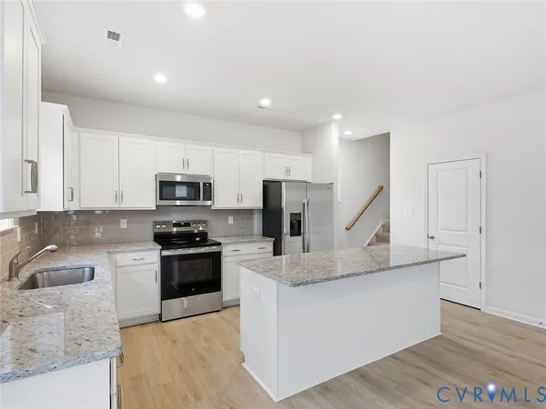 a white kitchen with stainless steel appliances granite countertop a sink a stove top oven a refrigerator and dishwasher