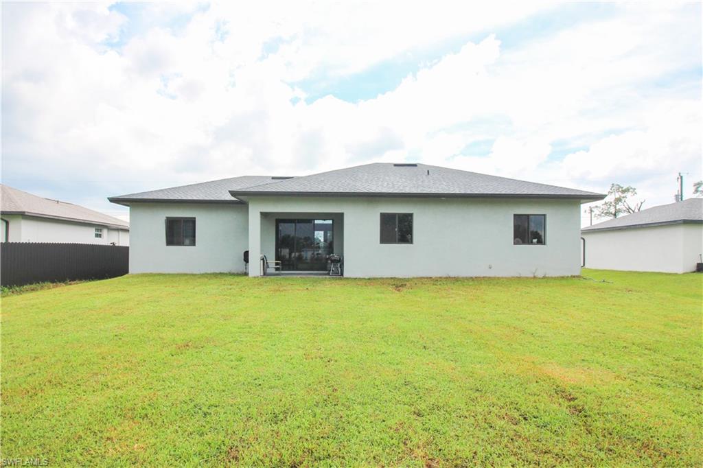 3902 4th Street Southwest Lehigh Acres, FL 33976 - Photo 30 of 34 Expansive green lawn, dark-toned privacy fencing, and a covered patio with sliding glass doors