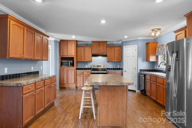 a kitchen with stainless steel appliances granite countertop a refrigerator a stove top oven a sink dishwasher and wooden cabinets with wooden floor