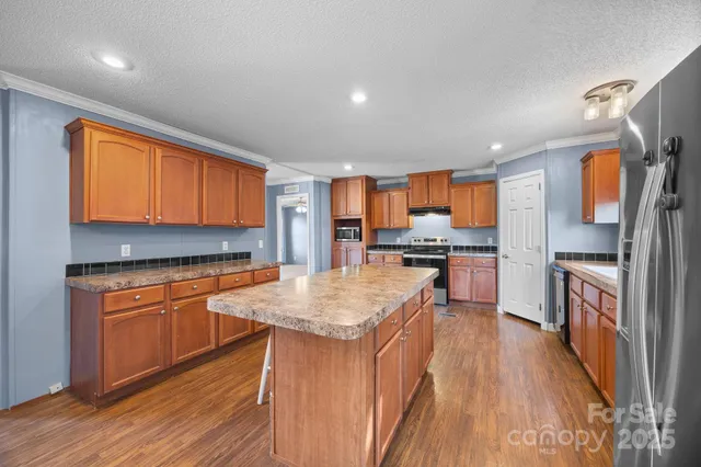 a kitchen with stainless steel appliances granite countertop a refrigerator a sink dishwasher a stove and white countertops with wooden floor