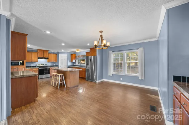 a kitchen with stainless steel appliances granite countertop a refrigerator a stove top oven and a dining table with wooden floor