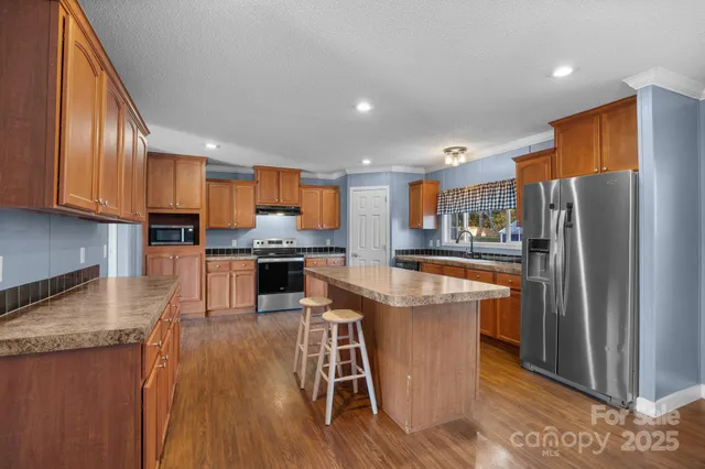 a kitchen with stainless steel appliances granite countertop a refrigerator a stove top oven a sink dishwasher and wooden cabinets with wooden floor