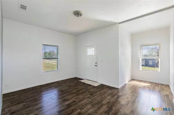 a view of an empty room with wooden floor and a window