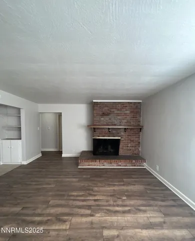 a view of an empty room with wooden floor fireplace and a window