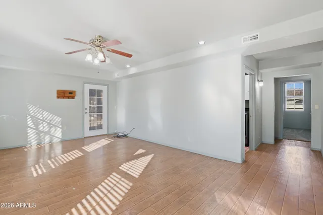 a view of an empty room with wooden floor and a ceiling fan