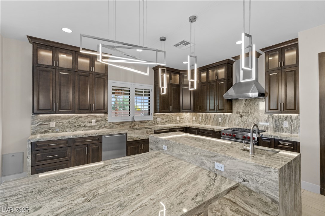 9865 Bright Angel Way Las Vegas, NV 89149 - Photo 23 of 98 Kitchen featuring wall chimney exhaust hood, appliances with stainless steel finishes, dark brown cabinetry, a sink, and light stone countertops