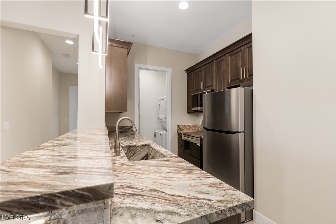 9865 Bright Angel Way Las Vegas, NV 89149 - Photo 66 of 98 Casita 1 Kitchen featuring stacked washer and clothes dryer, a sink, appliances with stainless steel finishes, dark brown cabinetry, and a peninsula
