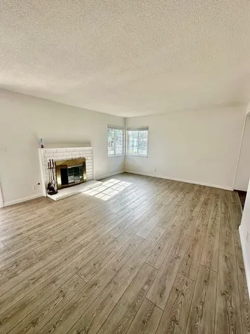 an empty room with wooden floor fireplace and windows
