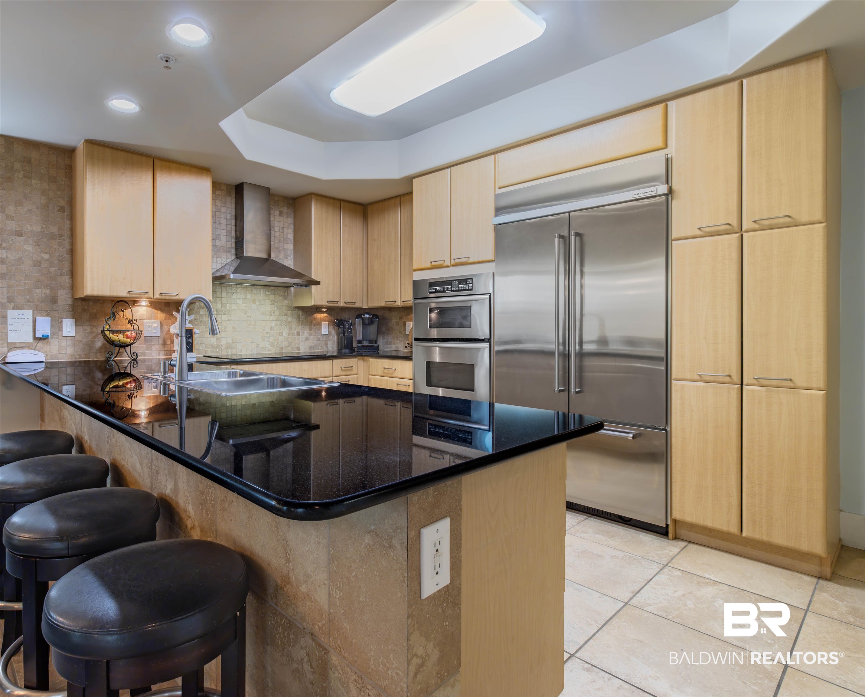 28107 Perdido Beach Boulevard, Unit D714 Orange Beach, AL 36561 - Photo 21 of 88 Kitchen with backsplash, a breakfast bar area, a peninsula, stainless steel appliances, and wall chimney exhaust hood