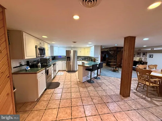 a kitchen with stainless steel appliances kitchen island granite countertop a refrigerator a stove a sink a dining table and chairs with wooden floor
