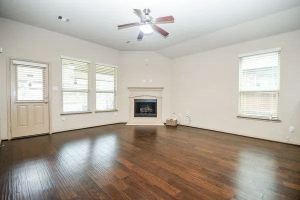 an empty room with wooden floor chandelier fan and windows