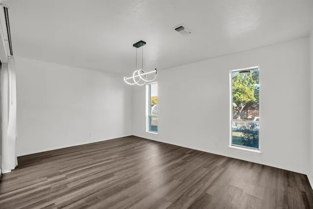 an empty room with wooden floor chandelier and windows