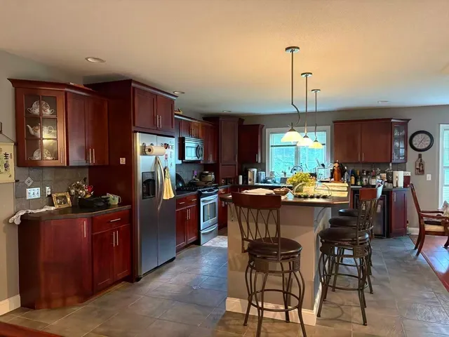 a kitchen with stainless steel appliances kitchen island granite countertop a refrigerator a stove a sink a dining table and chairs with wooden floor