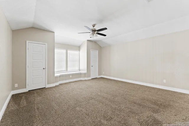 an empty room with chandelier fan and windows