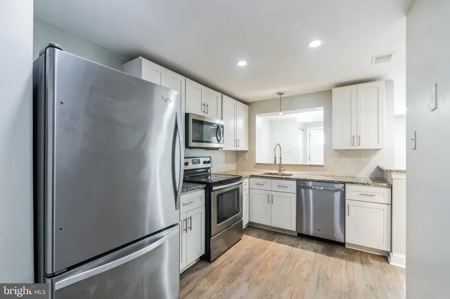 a kitchen with stainless steel appliances granite countertop white cabinets a refrigerator a sink a stove a microwave and wooden floors