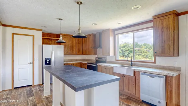 a kitchen with stainless steel appliances granite countertop a refrigerator a sink dishwasher a stove and white countertops with wooden floor