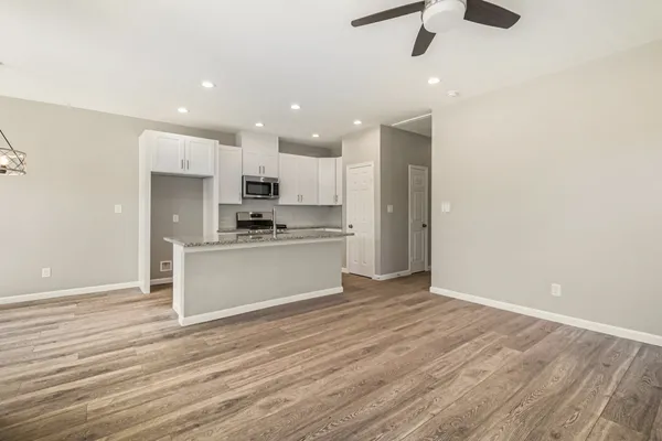 an empty room with wooden floor kitchen view and a window