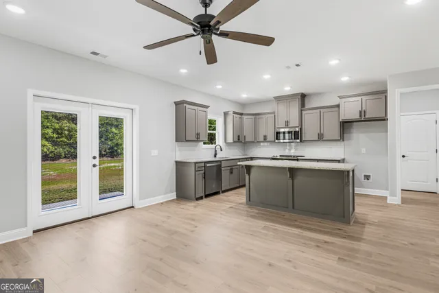 a large kitchen with stainless steel appliances granite countertop a stove a sink a refrigerator and white cabinets with wooden floor