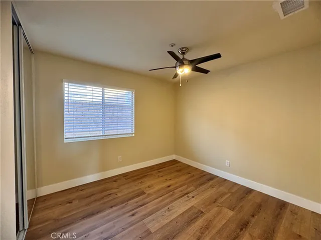 an empty room with wooden floor fan and windows