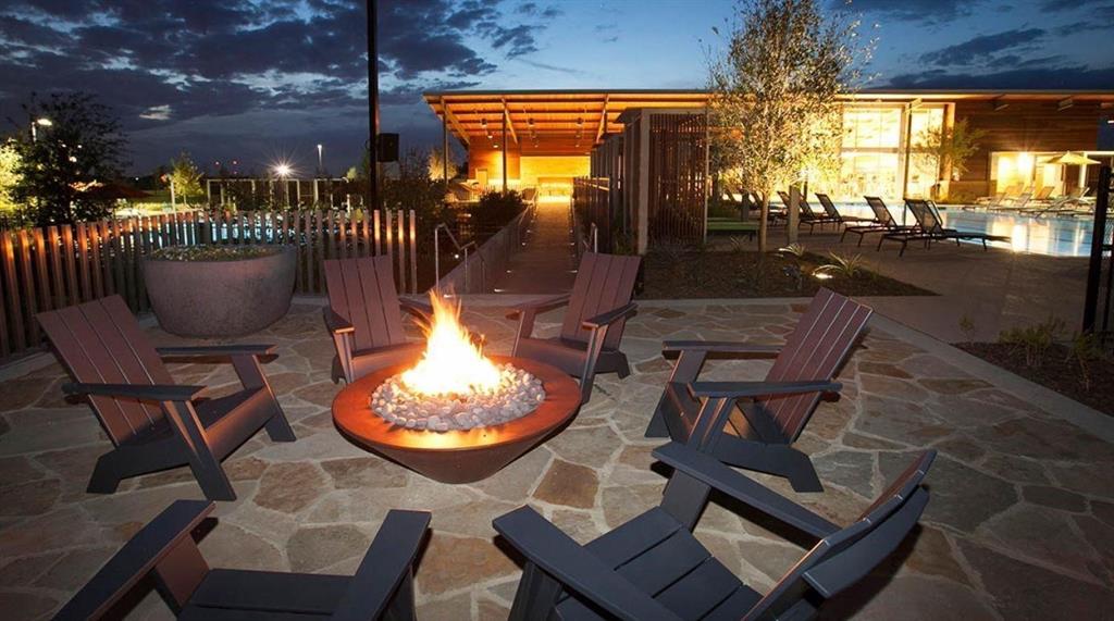 1000 Adair Road Prosper, TX 75078 - Photo 37 of 37 Outdoor stone-paved patio featuring a built-in fire pit, surrounded by a slatted wood fence, with a swimming pool and building structure in the background