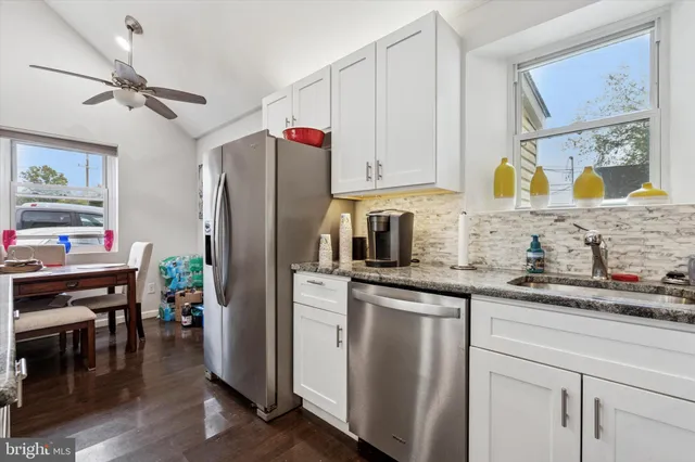 a kitchen with stainless steel appliances granite countertop a refrigerator a sink dishwasher and white cabinets with wooden floor