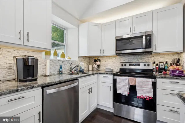 a kitchen with stainless steel appliances granite countertop grey cabinets a stove a sink and a microwave