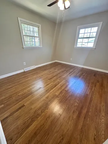 a view of an empty room with wooden floor and a chandelier fan