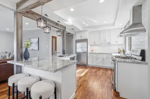 a kitchen with stainless steel appliances kitchen island granite countertop a stove a sink a refrigerator and white cabinets with wooden floor