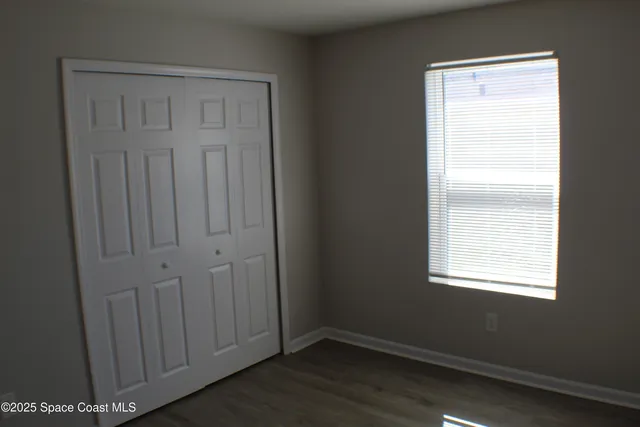 an empty room with wooden floor closet and windows