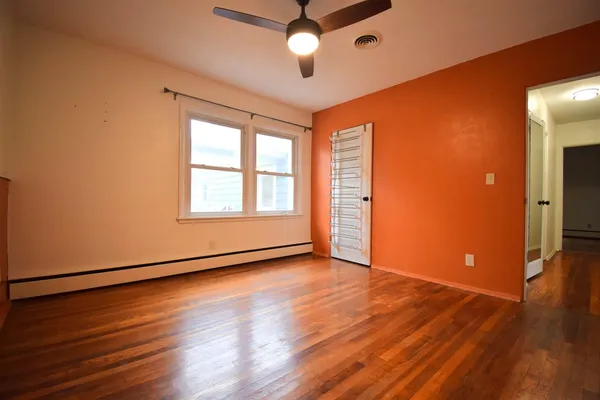 an empty room with wooden floor chandelier fan and windows