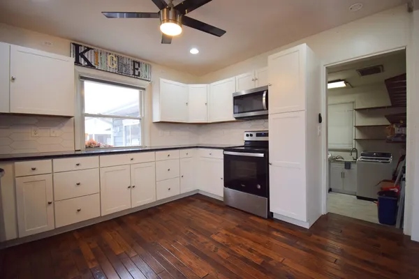 a kitchen with stainless steel appliances granite countertop a stove a sink and white cabinets with wooden floor next to windows