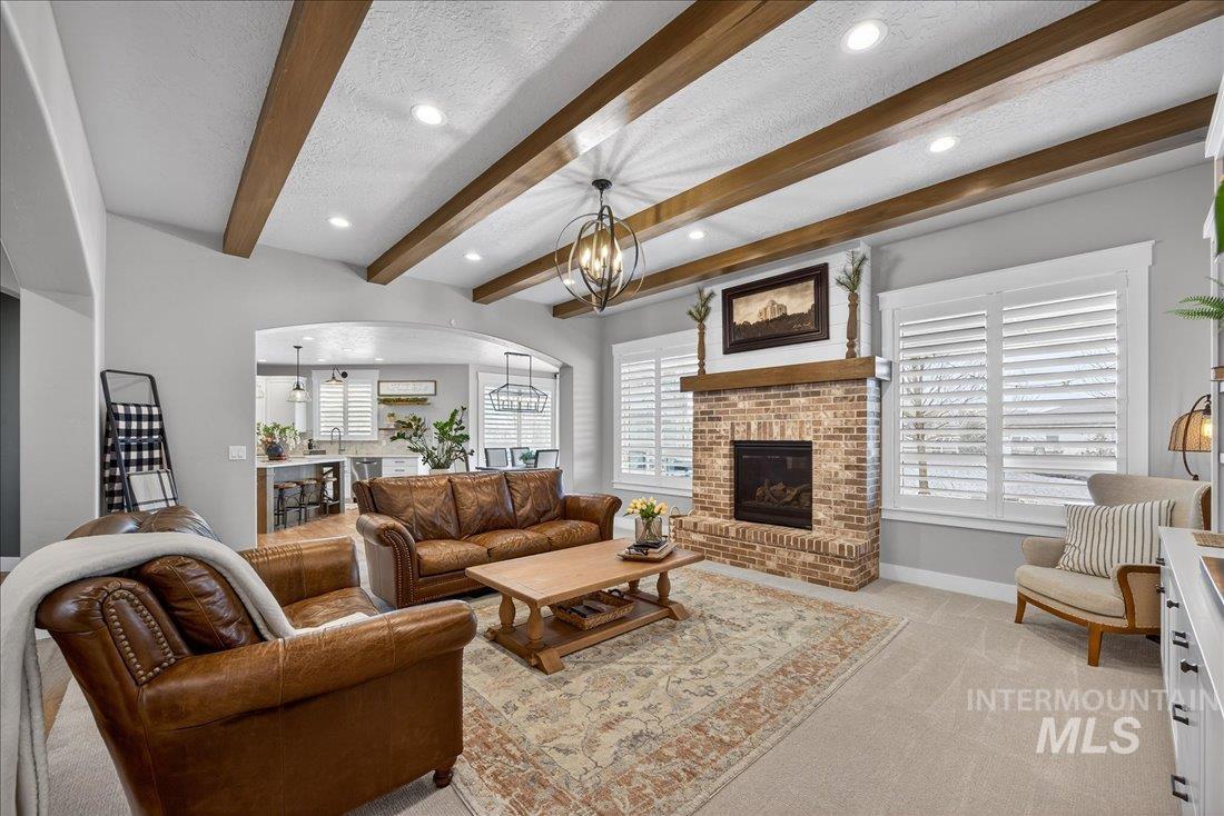 15111 Pinehurst Way Caldwell, ID 83607 - Photo 4 of 43 Living area with a fireplace, light carpet, arched walkways, beamed ceiling, and a chandelier