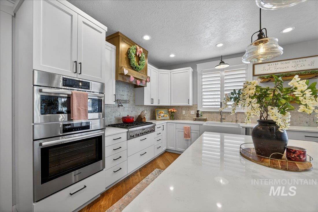 15111 Pinehurst Way Caldwell, ID 83607 - Photo 6 of 43 Kitchen with stainless steel appliances, white cabinetry, light stone countertops, wood finished floors, and a textured ceiling