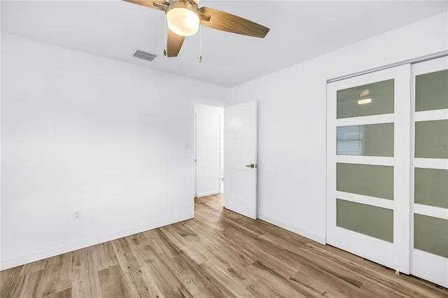 an empty room with wooden floor fan and windows