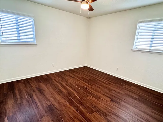 an empty room with wooden floor fan and windows