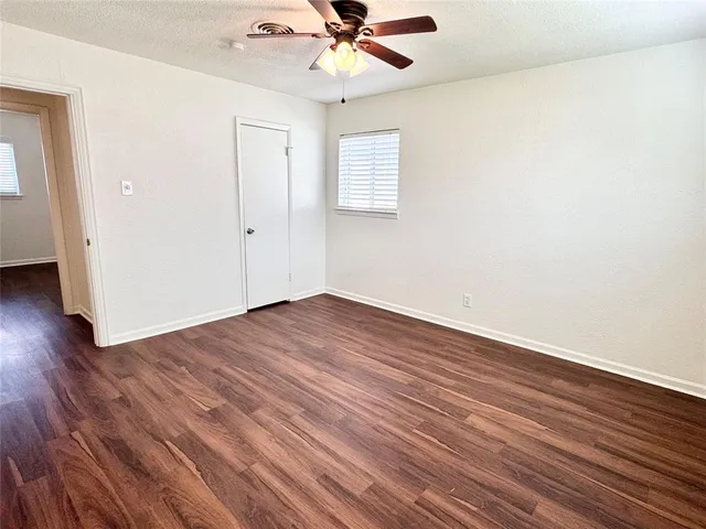 an empty room with wooden floor chandelier fan and windows